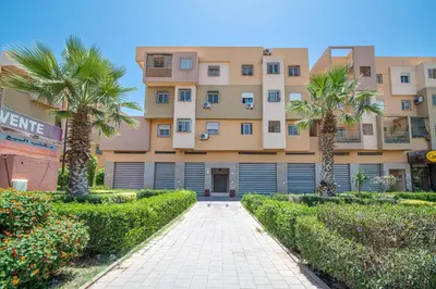 an apartment building with palm trees and a sidewalk at Appartement 2 chambre 5min Aéroport in Marrakech