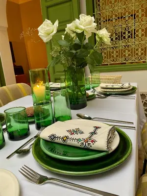 a table with green plates and a vase with white roses at Riad Dar Adal exclusivité 2 à 6 personnes petit déjeuner compris place jemaa El fna in Marrakech