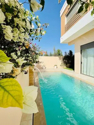 a swimming pool in front of a building with flowers at Villa LEONARDO Piscine & Rooftop Terrase in Marrakech