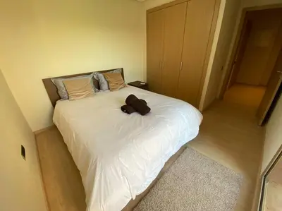 a bedroom with a white bed with a brown object on it at BEL APPART FONCTIONNEL PRESTIGIA GOLF MARRAKECH in Marrakech