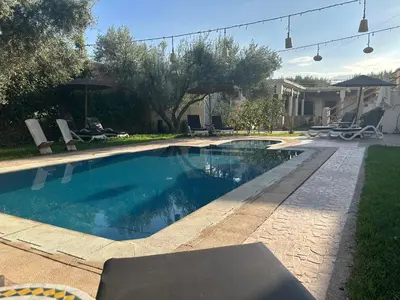 a swimming pool in a yard with chairs and umbrellas at Oasis Merasi Marrakech in Marrakech