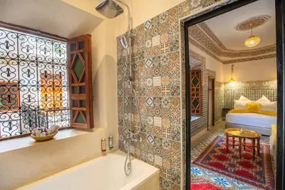 a bathroom with a tub and a bed and a window at Riad Albaraka in Marrakech