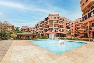 a swimming pool with a fountain in front of a building at Appartement véranda marrakech in Marrakech