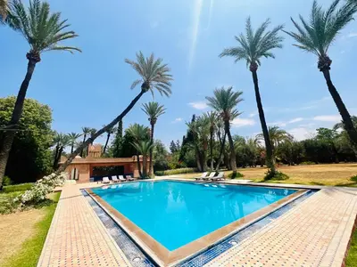 a pool with palm trees in front of a house at Majestic Luxury Villa Marrakech in Marrakech