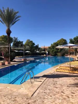 a large swimming pool with a palm tree and umbrellas at Palmeraie Village 2 - Cosi appartement en Rez de Jardin in Marrakech