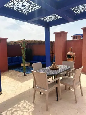 a patio with a table and chairs under a blue umbrella at Vizir Center Appartement avec solarium in Dar Caïd Layadi