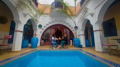 three people sitting at a table next to a swimming pool at Riad Safir Marrakech in Marrakech