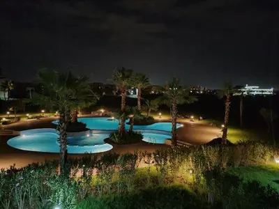 a group of pools with palm trees at night at Appartement Prestigia Golf City Marrakech - Porte Agate - Gated community Rez-de-Jardin in Marrakech