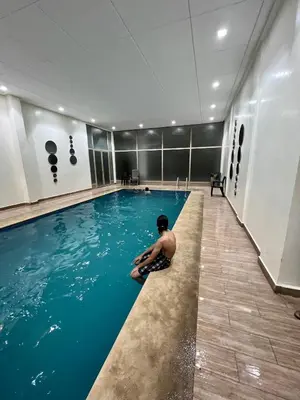a man sitting on the edge of a swimming pool at Apparemment deux chambres salon 16 in Marrakech