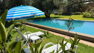a pair of chairs and an umbrella next to a swimming pool at Le Domaine des Oliviers in Marrakech