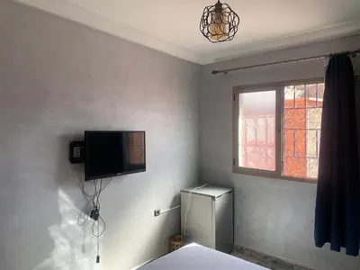 a room with a refrigerator and a tv on the wall at Familiale Chambre calm wifi Hanae in Marrakech