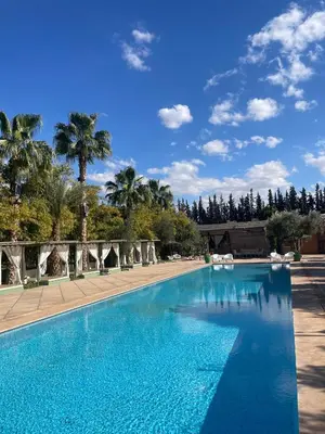 a blue swimming pool with palm trees in the background at Le Bled Ferme in Marrakech