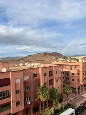 an apartment building with palm trees and a hill in the background at Appartement Marrakech Gueliz 5 Min Drive to City Center in Marrakech