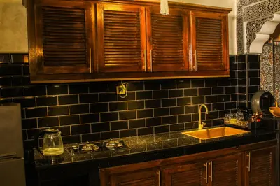 a kitchen with a sink and a black tiled wall at Appartement style Riad, 2 chambres, ambiance cosy in Marrakech