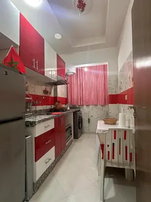 a kitchen with red cabinets and a table in it at Charmant Appartement 2 Chambres pour Sejours en Famille Marrakech in Marrakech