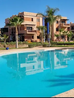 a swimming pool in front of a building with palm trees at Appartement paisible et abordable Palmeraie Marrakech in Dar Caïd Layadi