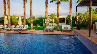 a swimming pool with chairs and palm trees at Luxury heated pool Villa Marrakech in Marrakech