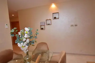 a glass table with a vase of flowers and chairs at Appartement Prestigia Golf City Marrakech in Marrakech