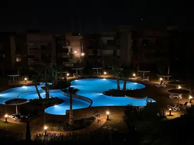 a large blue pool with tables and umbrellas at night at New appart, pool and golf view in Marrakech