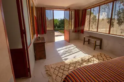 a room with a bed and a table and windows at La Ferme de LallaDom in Tameslouht