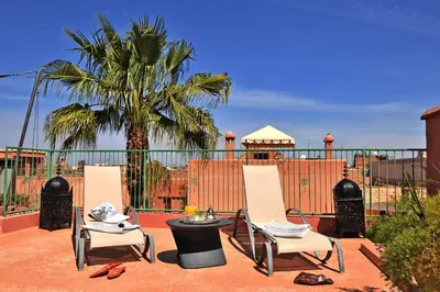 two chairs and a table on a patio with a palm tree at Riad L'Aziza in Marrakech
