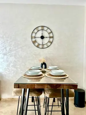a table with chairs and a clock on the wall at Cosy appartement au Domaine de Noria in Marrakech