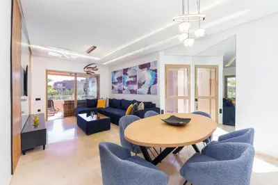 a living room with a table and blue chairs at Luxueux appartement prestigia golf/vue piscine in Marrakech