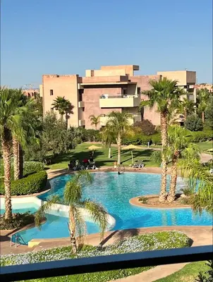 a swimming pool with palm trees in front of a building at Prestigia Golf Vue Atlas et Piscine in Marrakech