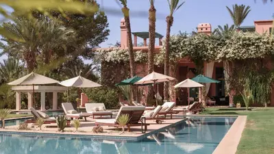 a pool with lounge chairs and umbrellas next to a house at Villa Prestige Mansourya in Marrakech