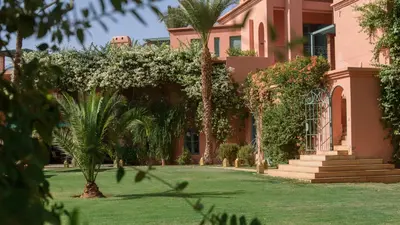 a pink house with palm trees and a yard at Villa Prestige Mansourya in Marrakech