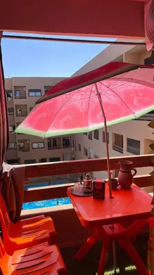 a red table with an umbrella next to a pool at appartement hivernage marrakech avec piscine in Marrakech