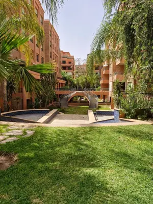 a park with a bridge and some grass and buildings at Appartement babylon 2 marrakech in Marrakech