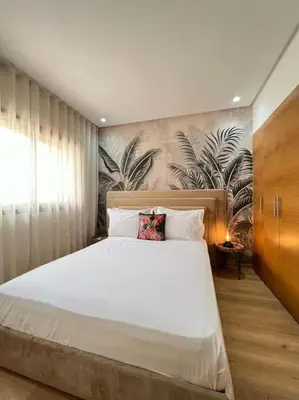 a bedroom with a large white bed with a tropical wallpaper at Appartement moderne au Golf in Marrakech