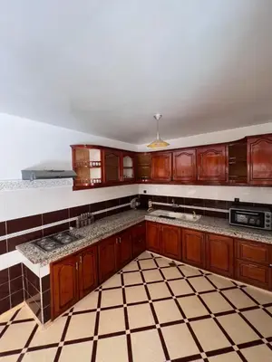 a kitchen with wooden cabinets and a tiled floor at Charmant appartement spacieux avec cour fleurie et Hammam à Targa Marrakech in Marrakech