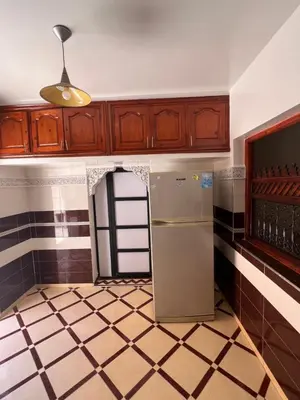 an empty kitchen with a refrigerator and wooden cabinets at Charmant appartement spacieux avec cour fleurie et Hammam à Targa Marrakech in Marrakech