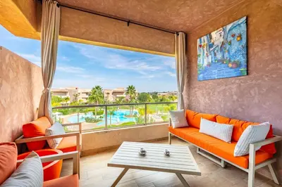 a living room with an orange couch and a large window at Appartement luxe Prestige Opale Golf in Marrakech