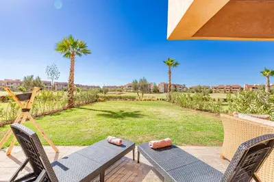 a patio with two chairs and a table and a lawn with palm trees at Résidence Golfique ,Piscine,Jardin terrasse privée in Marrakech