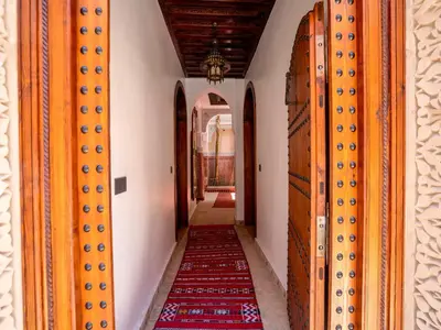 a corridor of a house with wooden doors and a red carpet at Belle Riad de médina in Marrakech