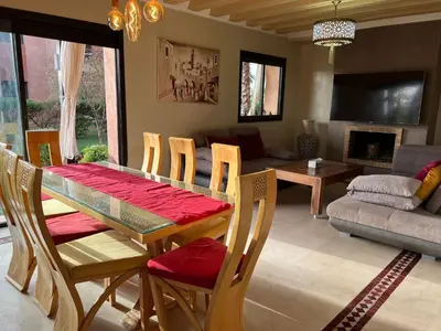 a dining room with a table and chairs and a living room at Appartement élégant avec vue sur piscine jardin verdoyant et wifi ultra rapide in Marrakech