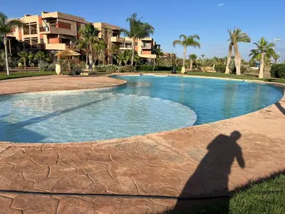 a shadow of a person standing in front of a swimming pool at Appartement élégant avec vue sur piscine jardin verdoyant et wifi ultra rapide in Marrakech