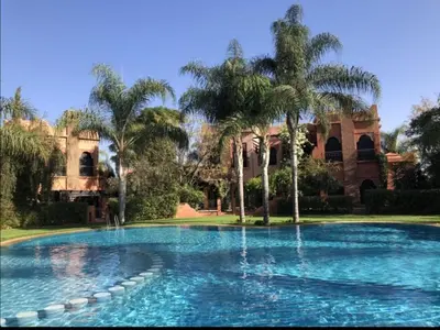 a swimming pool with palm trees in front of a building at Maison d'Hôte Angele in Sfiani