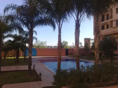 a swimming pool with palm trees in front of a building at Appartement Elias Marrakech in Marrakech