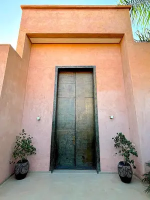 a door to a pink building with two potted plants at Palais Noor in Douar Caïd Layadi