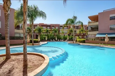 a swimming pool with palm trees in front of a building at Luxury Apartment in Marrakech in Marrakech