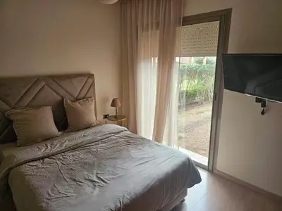 a bedroom with a bed and a large window at Bel appartement avec piscine et jardin in Marrakech