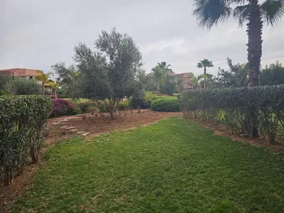 a garden with green grass and palm trees at Bel appartement avec piscine et jardin in Marrakech