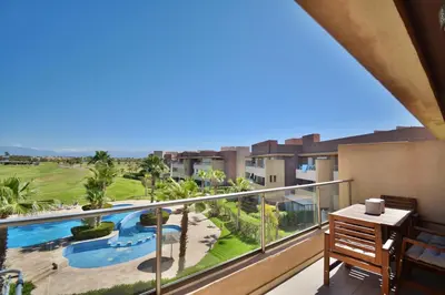 a balcony with a view of a pool and palm trees at Appartement Prestigia - Golf - Piscine - Restaurants in Marrakech
