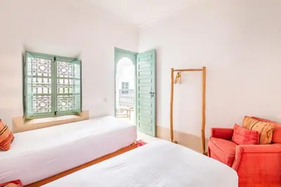 a bedroom with two beds and a red chair at Peaceful Oasis Authentic Riad in Marrakech