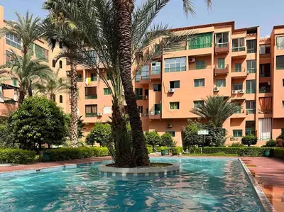 a swimming pool with a palm tree in front of a building at Appartement avec piscine Guéliz in Marrakech