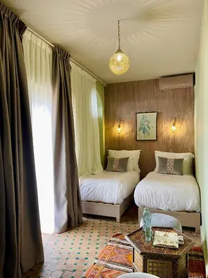 a room with two beds and a table and a window at Riad La Calèche in Marrakech